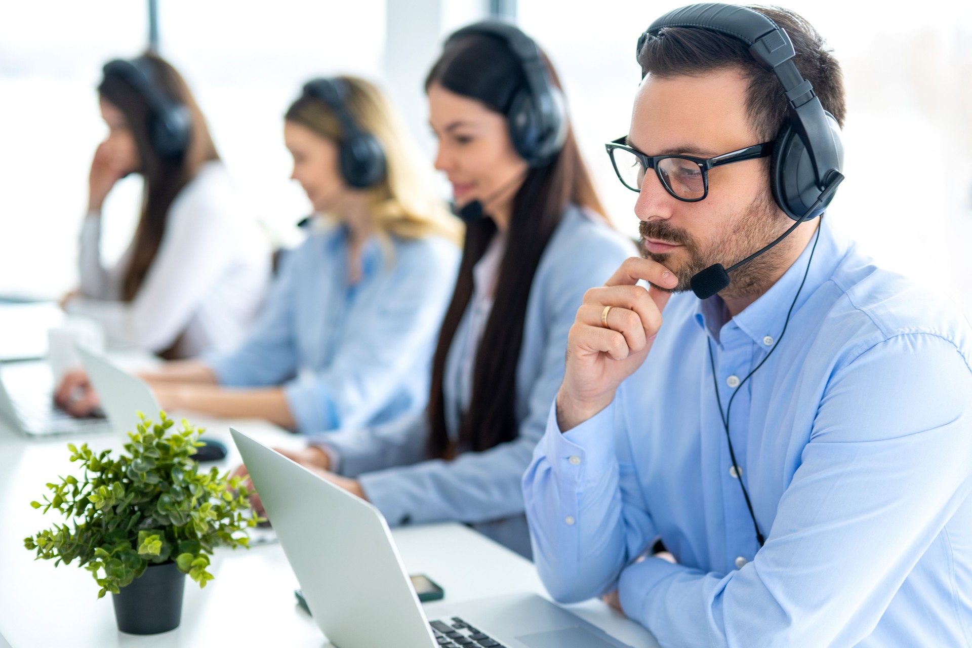 Serious call center agent in headset with microphone consulting and listening to client during phone call at call center